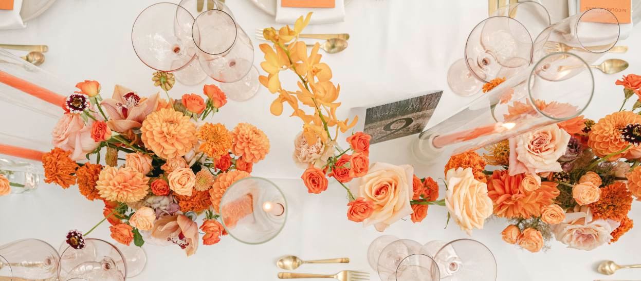 An overhead view of a citrus-toned reception table with orange and marigold florals and gold flatware